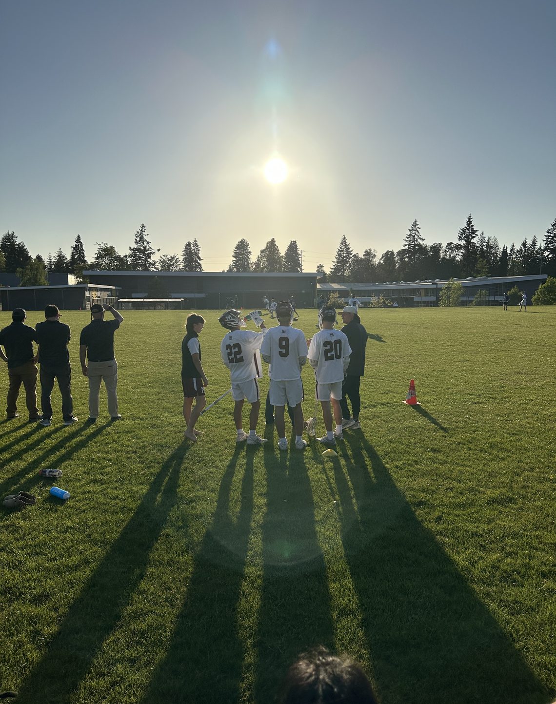 Three lacrosse players standing together on a field at sunset.