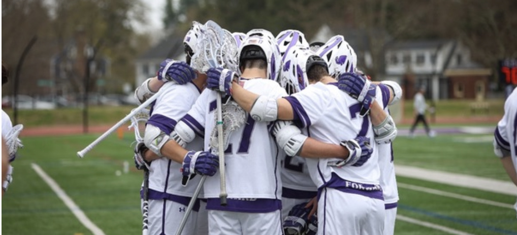 The Amherst Men's Lacrosse team huddled together on the field with their coaches.
